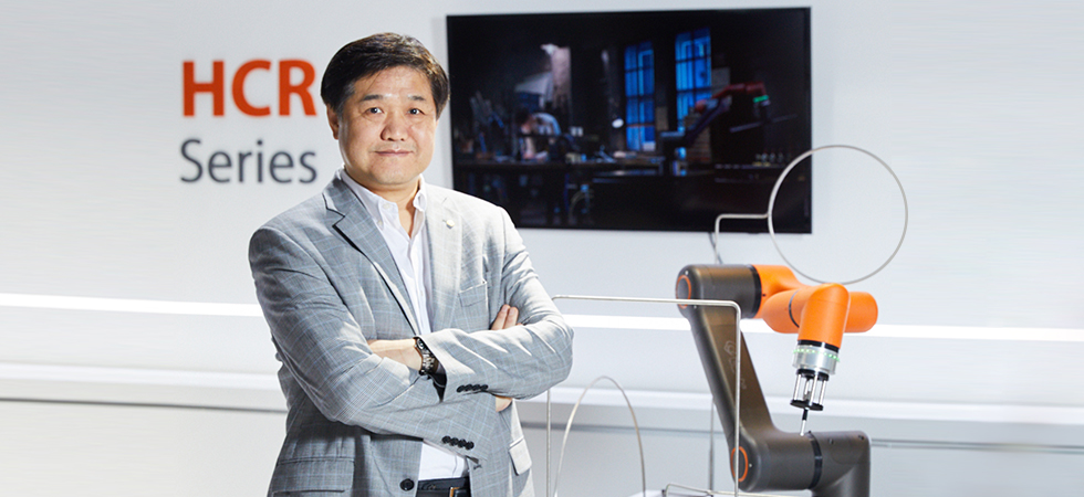 Woo Sok Chang, Executive Vice President of Hanwha Precision Machinery, proudly stands next to a HCR-3  collaborative robot as it performs a precision tracking demonstration.